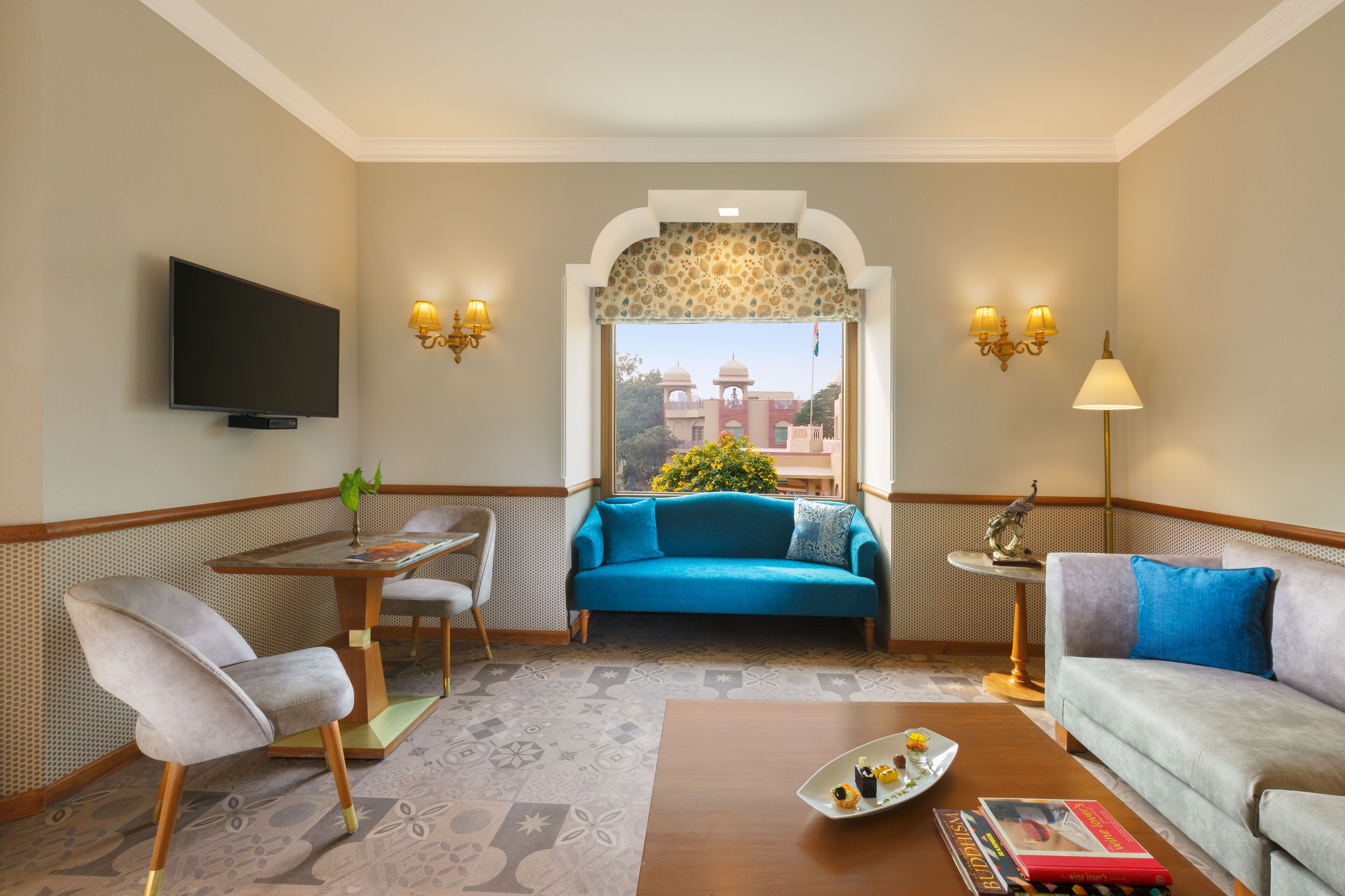 A hotel room with a sofa, armchair, and a small table with a tray of snacks.