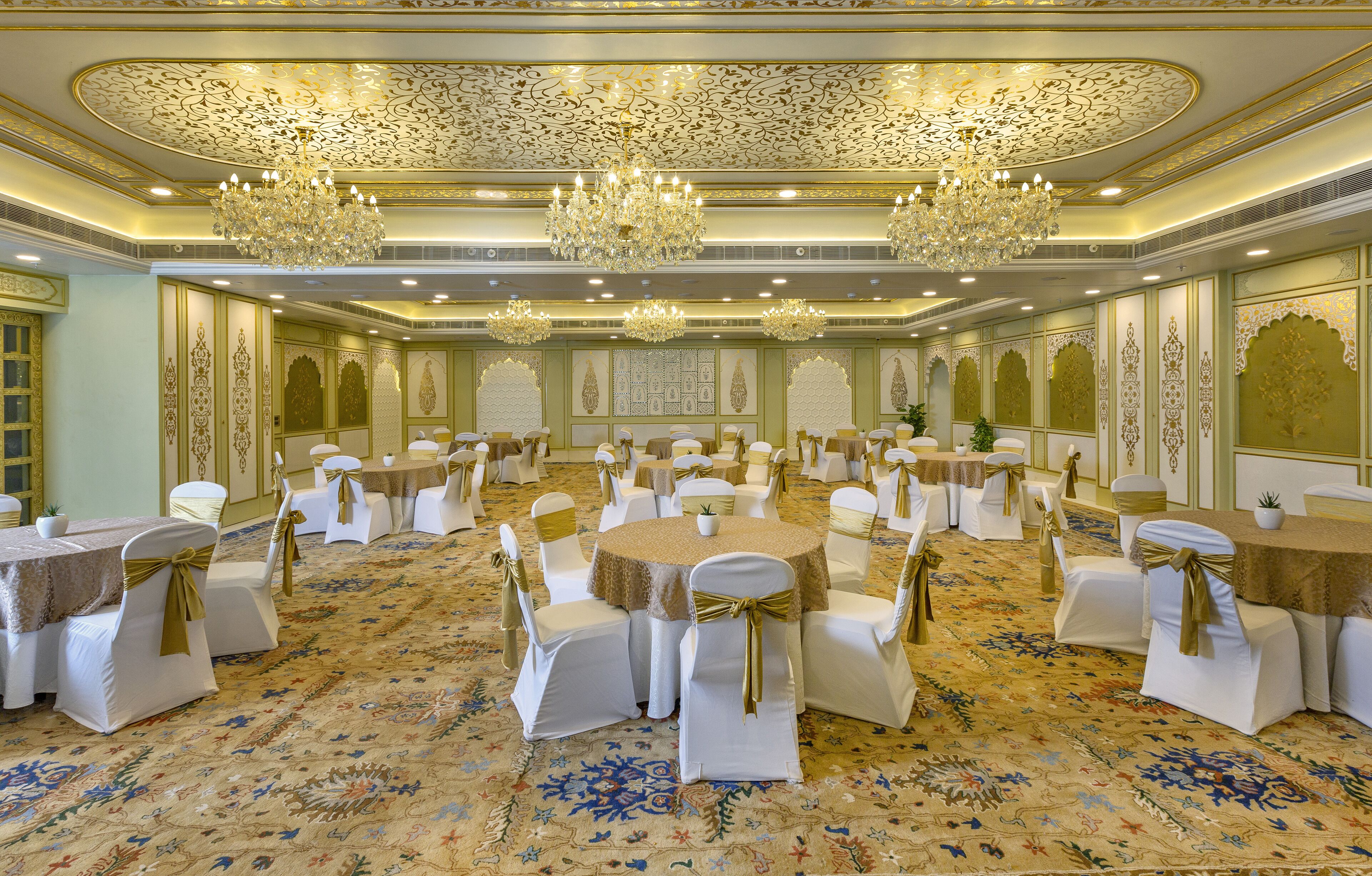 Un salón de banquetes con mesas redondas, sillas blancas y candelabros.