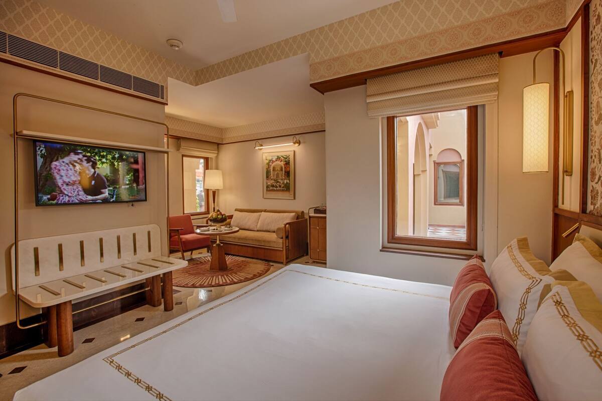 A hotel room with a large bed, a TV, a sofa, a small table, and a window with a view of the outside.