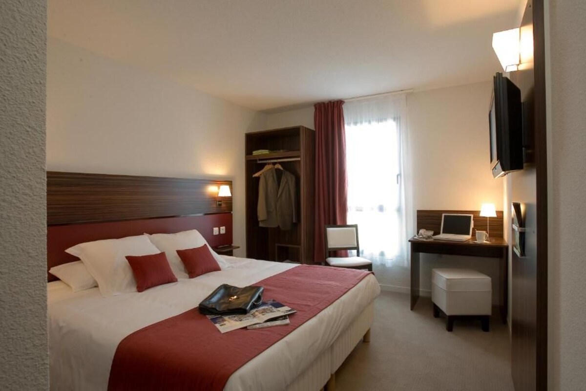 Ein Hotelzimmer mit Bett, Nachttisch, Schreibtisch, Stuhl, Fernseher und Kleiderschrank.