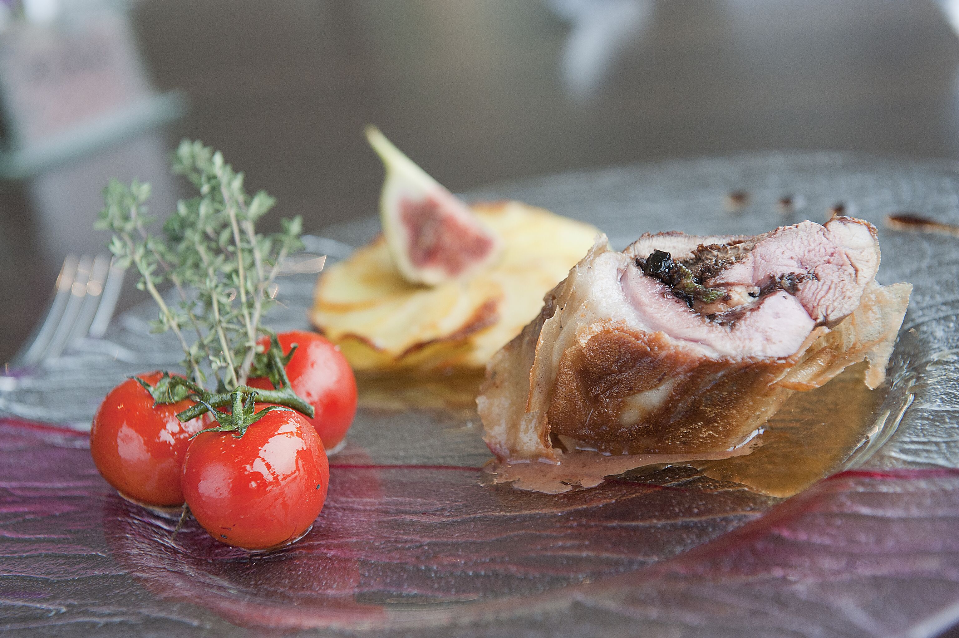 A glass plate with a piece of meat, a tomato, and a fig.