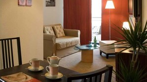 Mukava hotellihuone, jossa on sohva, ruokapöytä, jossa on kuppeja ja teekannu, lamppu ja kasvi.