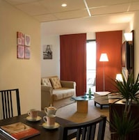 Una habitación de hotel acogedora con un sofá, una mesa de comedor con tazas y una tetera, una lámpara y una planta.