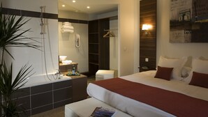 Moderni hotellihuone, jossa on suuri sänky, erillinen suihkutila, pieni oleskelualue ja kylpyammeella varustettu kylpyhuone.
