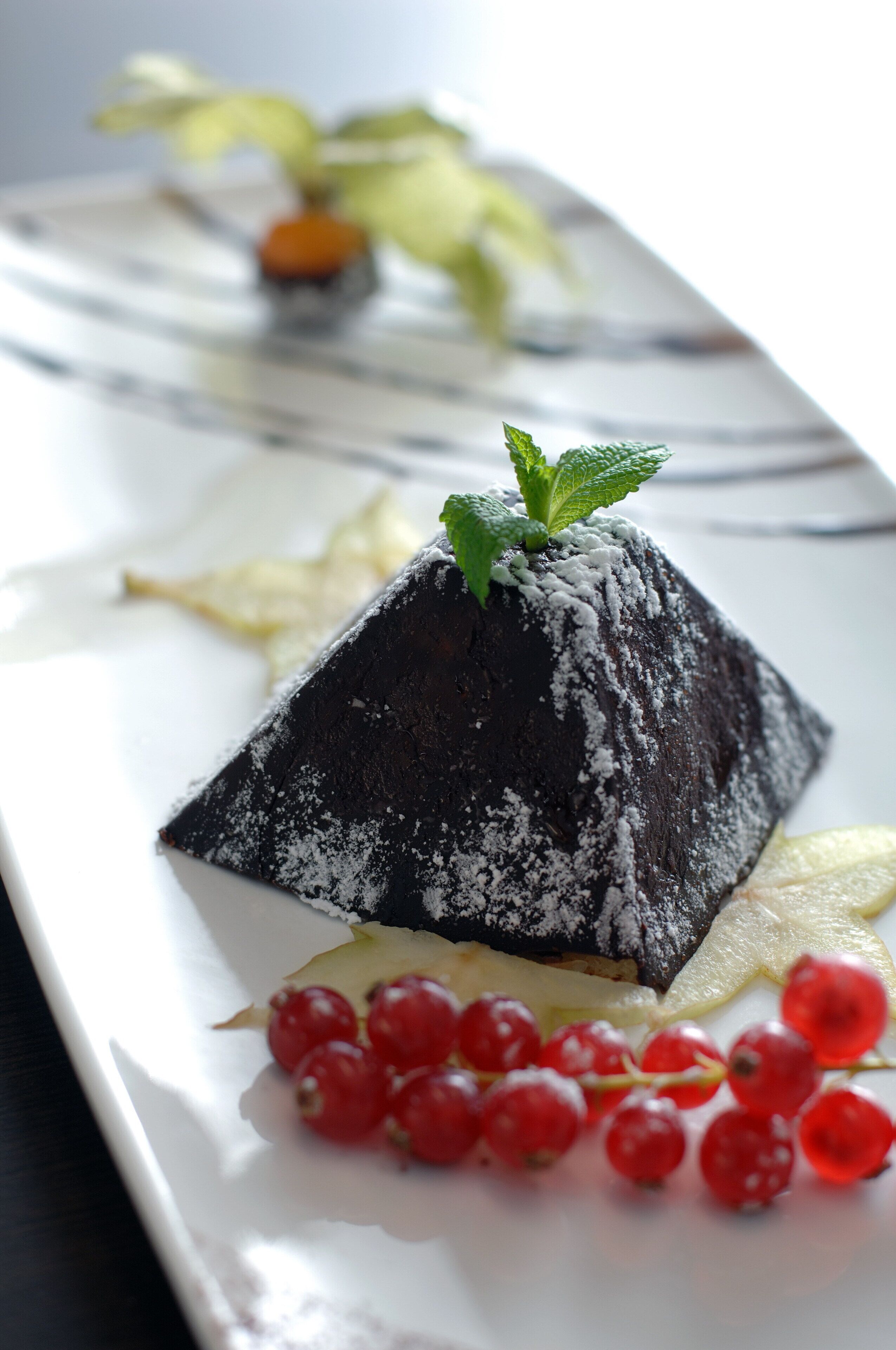 Un postre sobre un plato blanco con grosellas rojas y una hoja de menta como decoración.