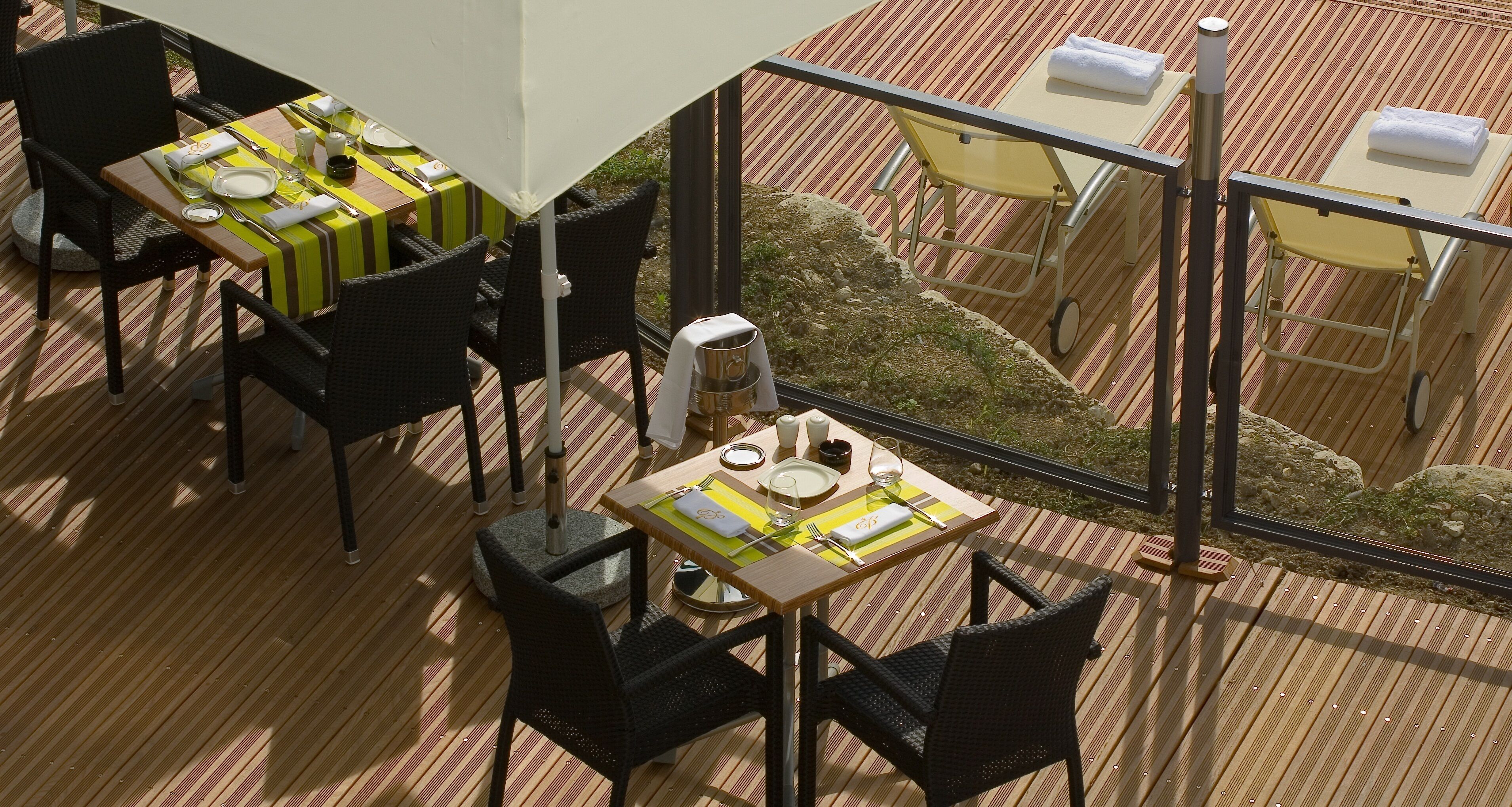 Un coin repas avec des tables préparées pour deux personnes, des chaises en osier noir et une vue sur le jardin grâce à de grandes fenêtres.