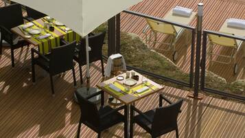 A dining area with tables set for two, black wicker chairs, and a view of the garden through large windows.