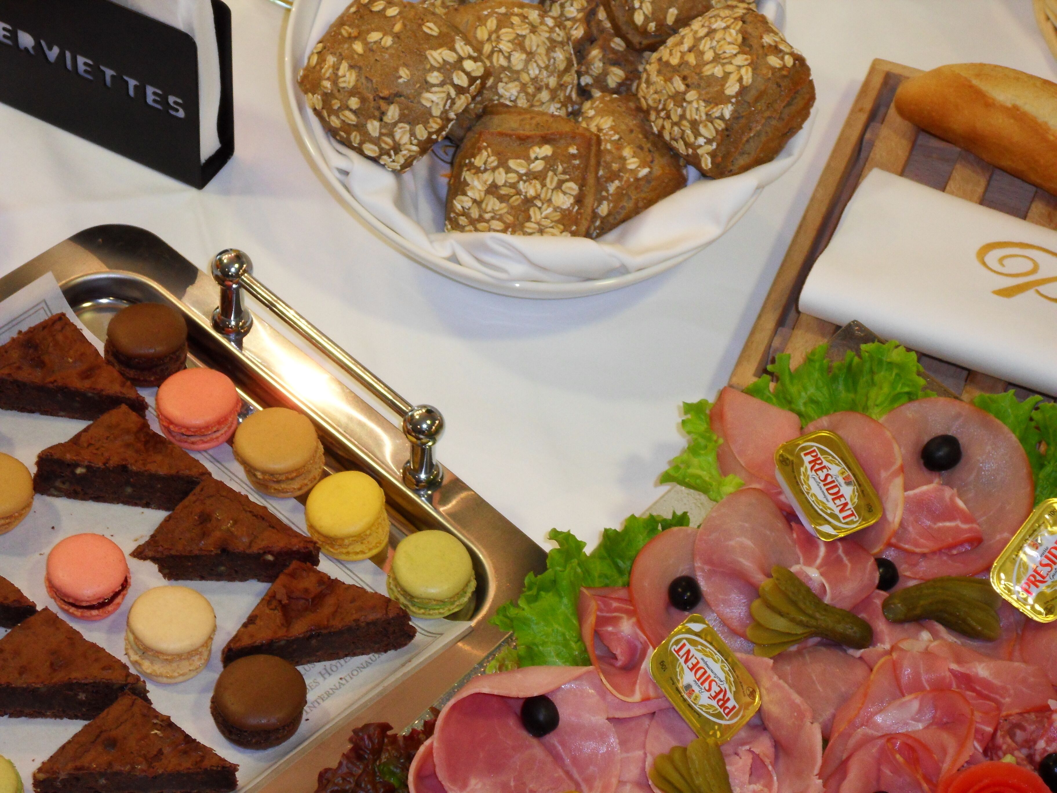 Un tavolo da buffet con diversi cibi, tra cui macarons, brownies e una selezione di carni e formaggi.