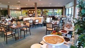 Moderni ravintola, jossa on useita ruokailutiloja, keskeisellä paikalla sijaitseva baari sekä monipuolinen valikoima ruokia ja juomia, jotka on esillä pöydillä.