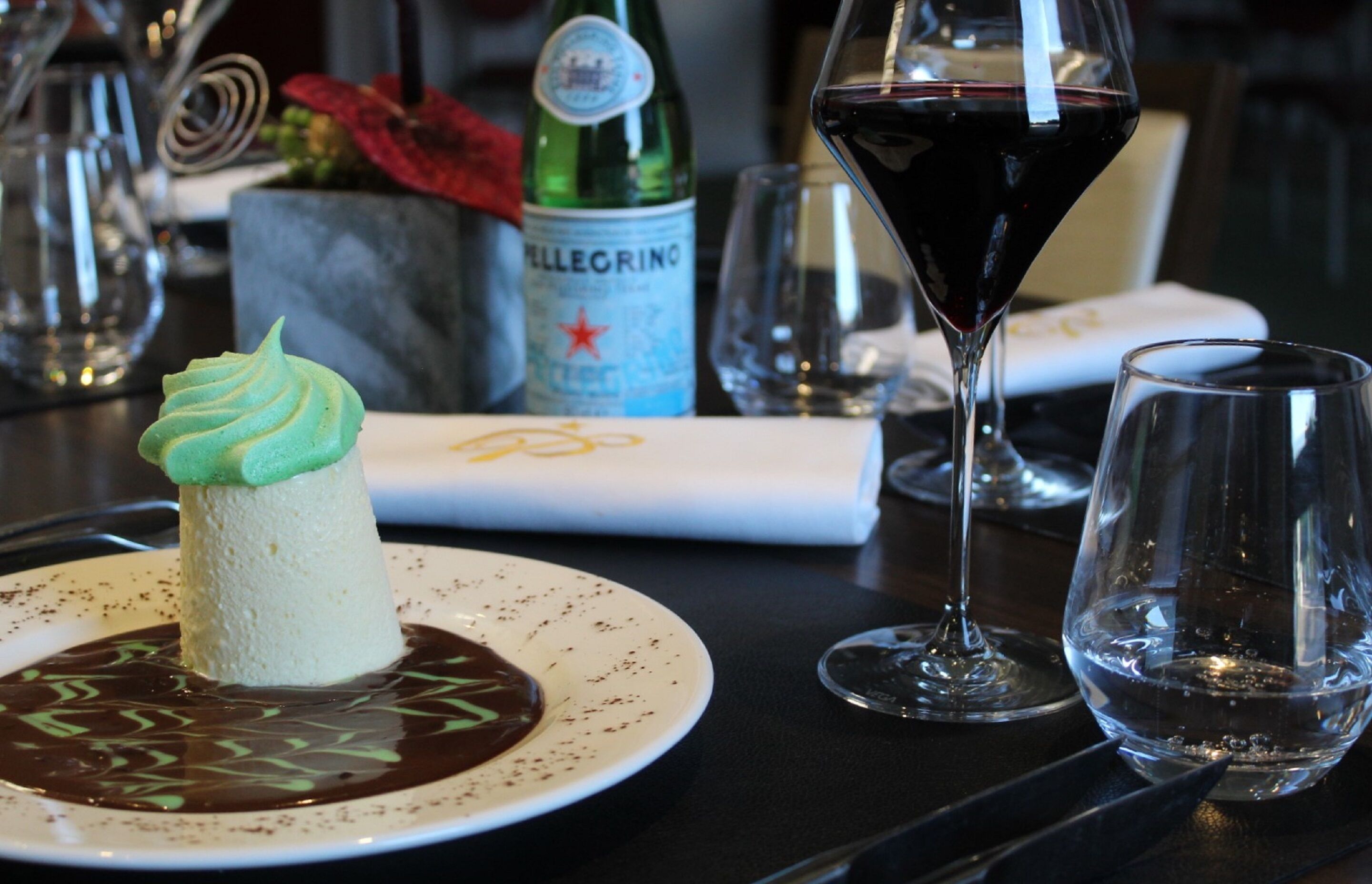 Un dessert présenté sur une assiette, accompagné d’une bouteille d’eau Pellegrino et d’un verre de vin rouge, le tout posé sur une table.