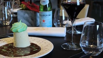 Un dessert présenté sur une assiette, accompagné d’une bouteille d’eau Pellegrino et d’un verre de vin rouge, le tout posé sur une table.