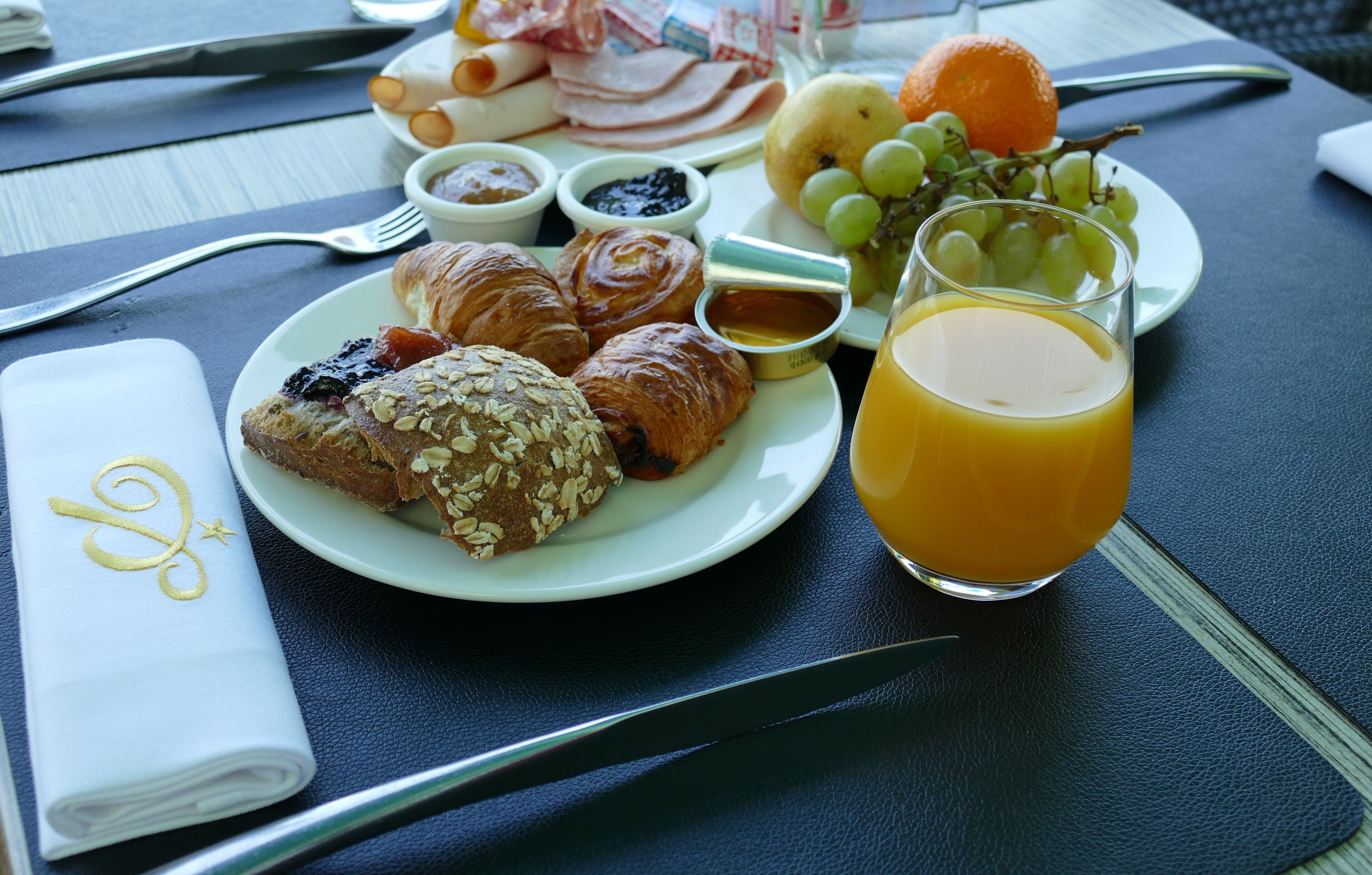 A breakfast setting with croissants, ham, eggs, and fruit on a table.