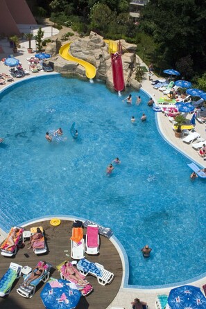 A large outdoor swimming pool with a water slide, lounge chairs, and umbrellas.