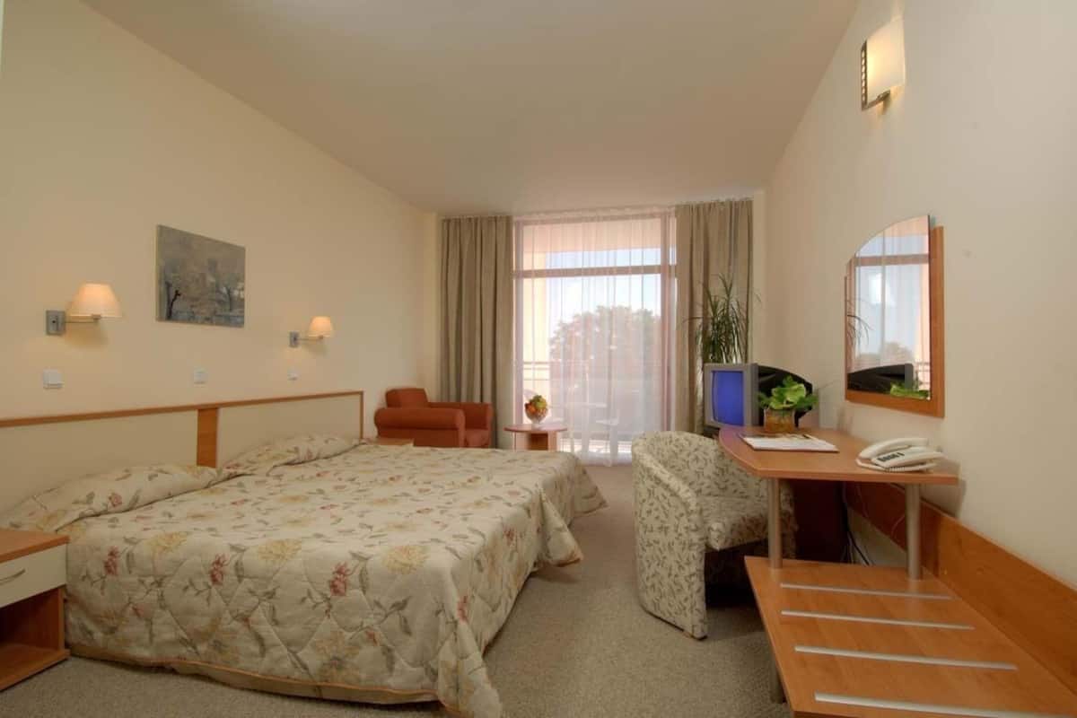 A hotel room with two beds, a desk with a telephone, a chair, a small table with a vase, and a window with curtains.
