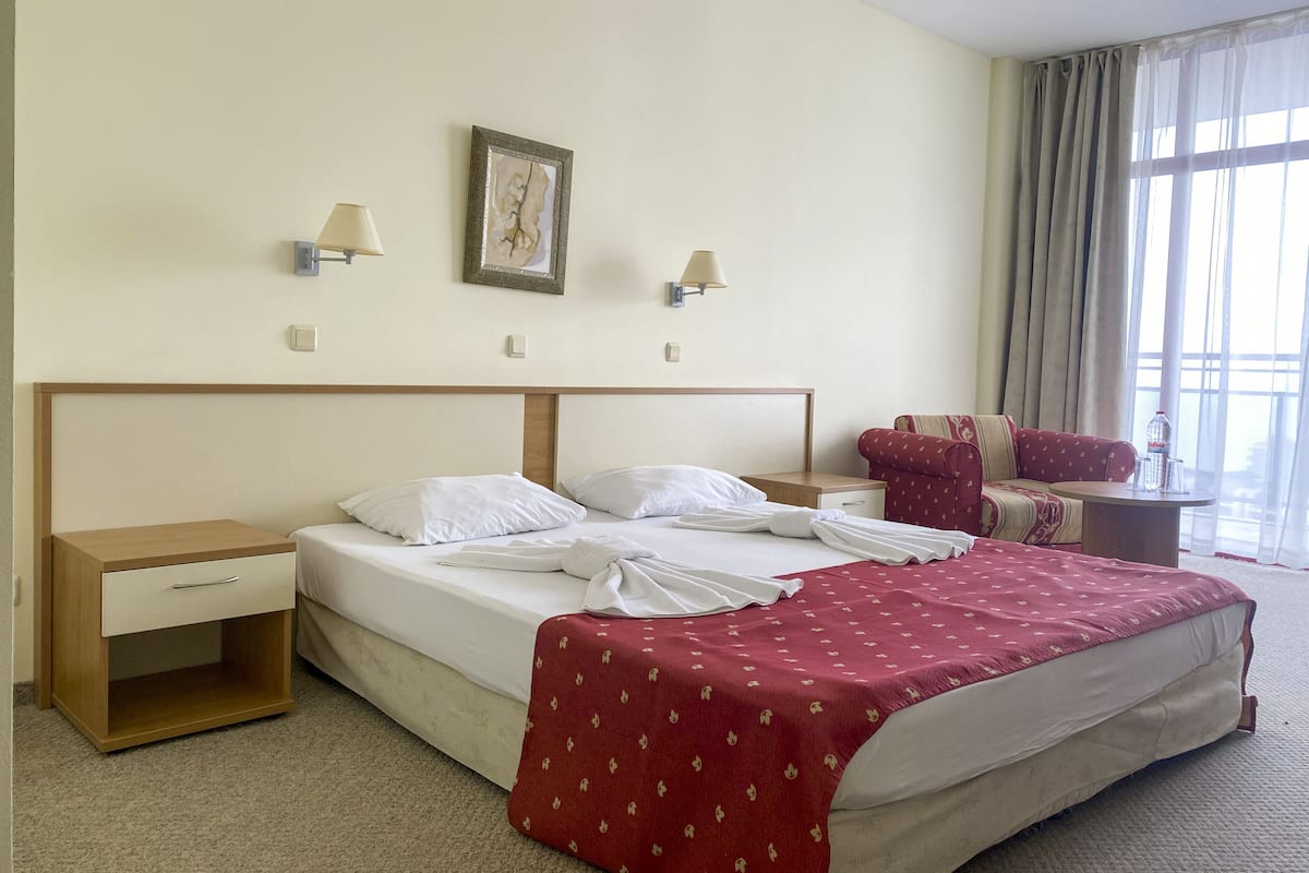 A hotel room with a bed, a nightstand, a chair, and a window with curtains.