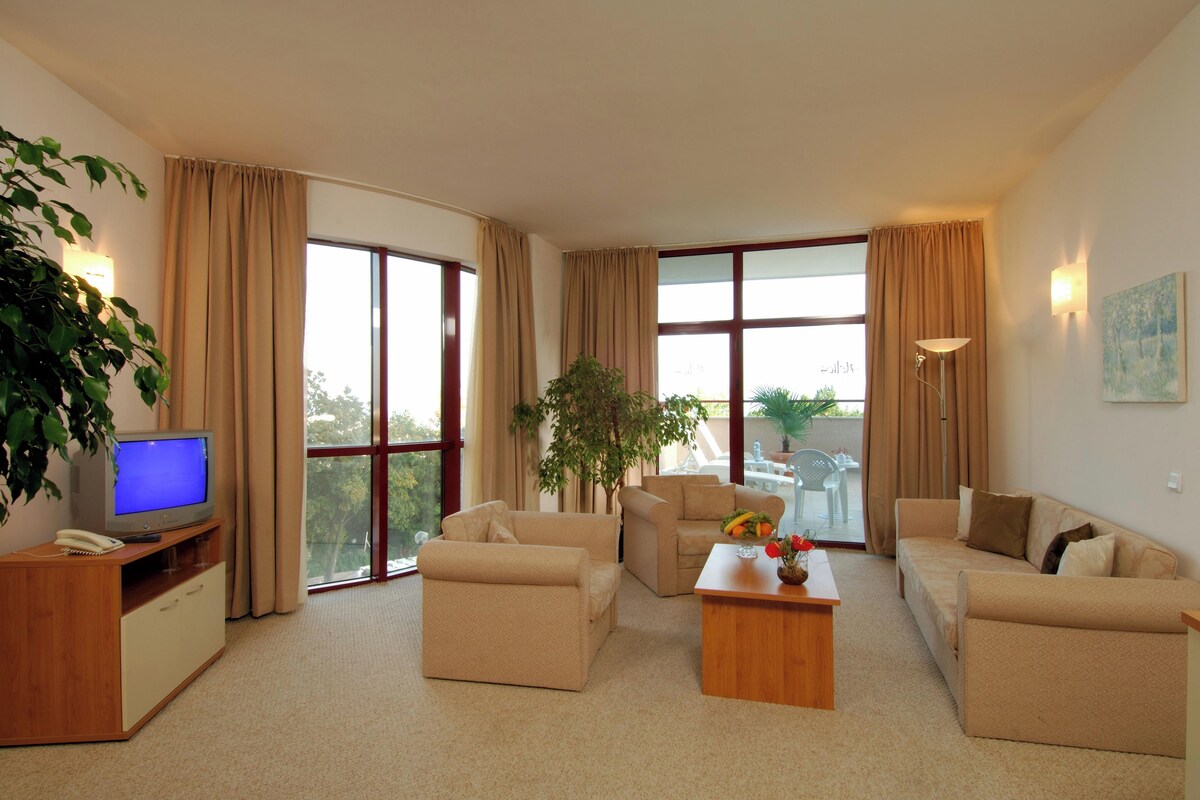 A living room with beige sofas, a coffee table, a TV, and a plant.