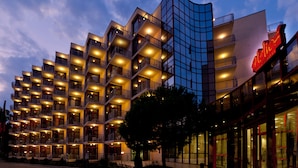 A multi-story hotel with balconies, a glass facade, and a red sign. - Helios Spa (Golden Sands)