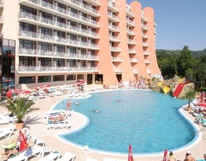Un hotel con una piscina grande, varios balcones y un ambiente de resort con tumbonas y sombrillas.