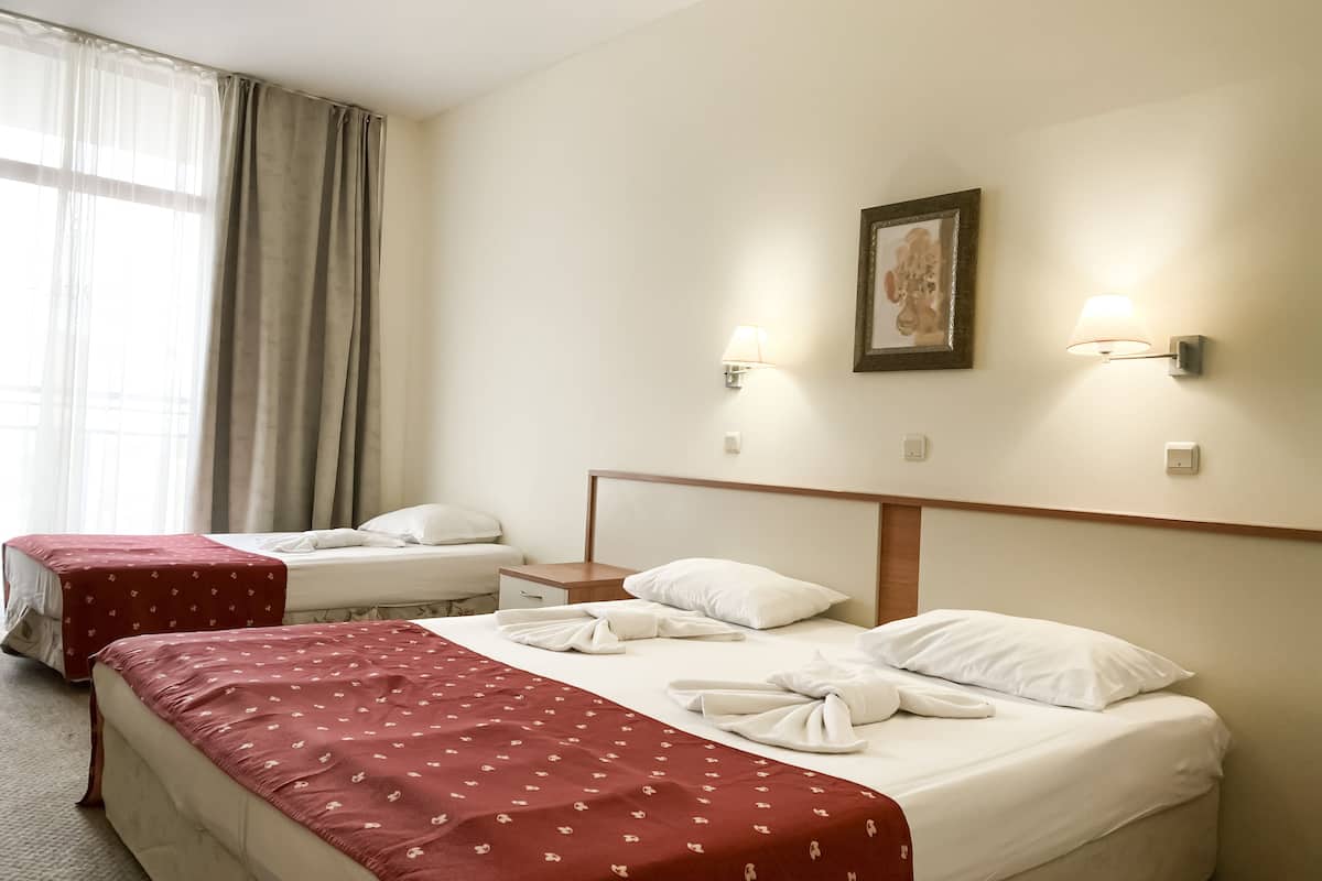 A hotel room with two beds, a nightstand, a wall-mounted lamp, and a framed picture.