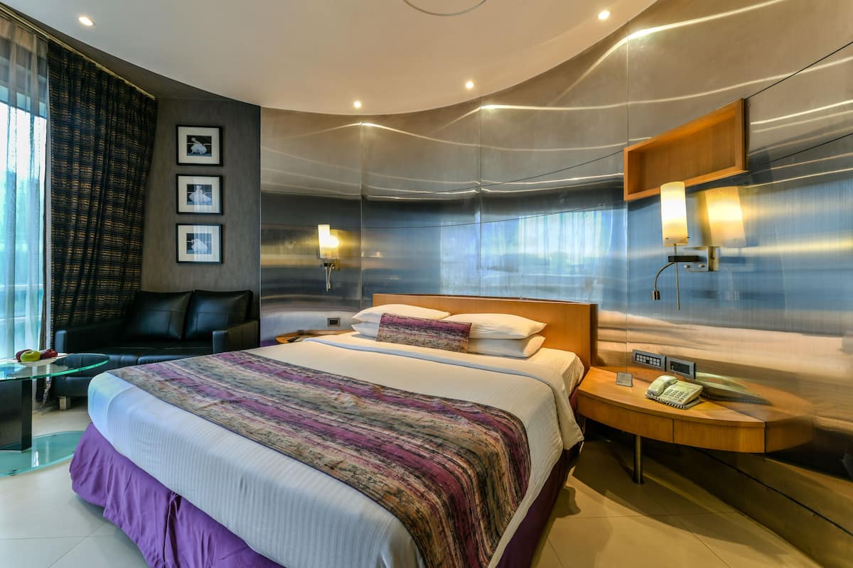 A modern hotel room with a large bed, a desk with a phone, and a chair.