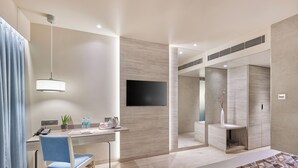 Une chambre d’hôtel moderne équipée d’un lit, d’un bureau, d’une chaise et d’un téléviseur fixé au mur.