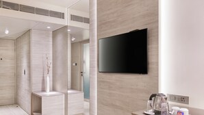 Une salle de bain moderne dotée d’un grand miroir, d’un téléviseur à écran plat fixé au mur et d’un coin café avec une bouilloire et des tasses.