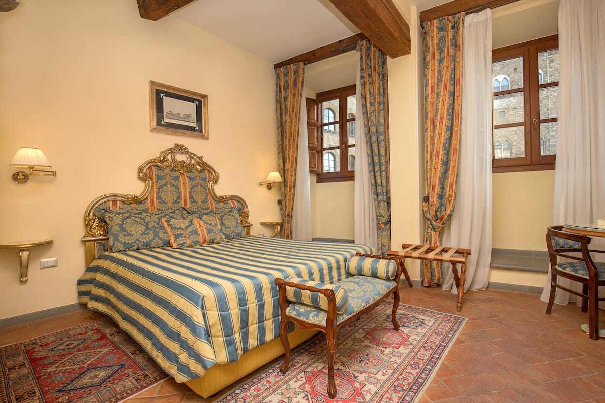 Une chambre à coucher avec un grand lit, un banc en bois, un bureau avec une chaise et un tapis à motifs.