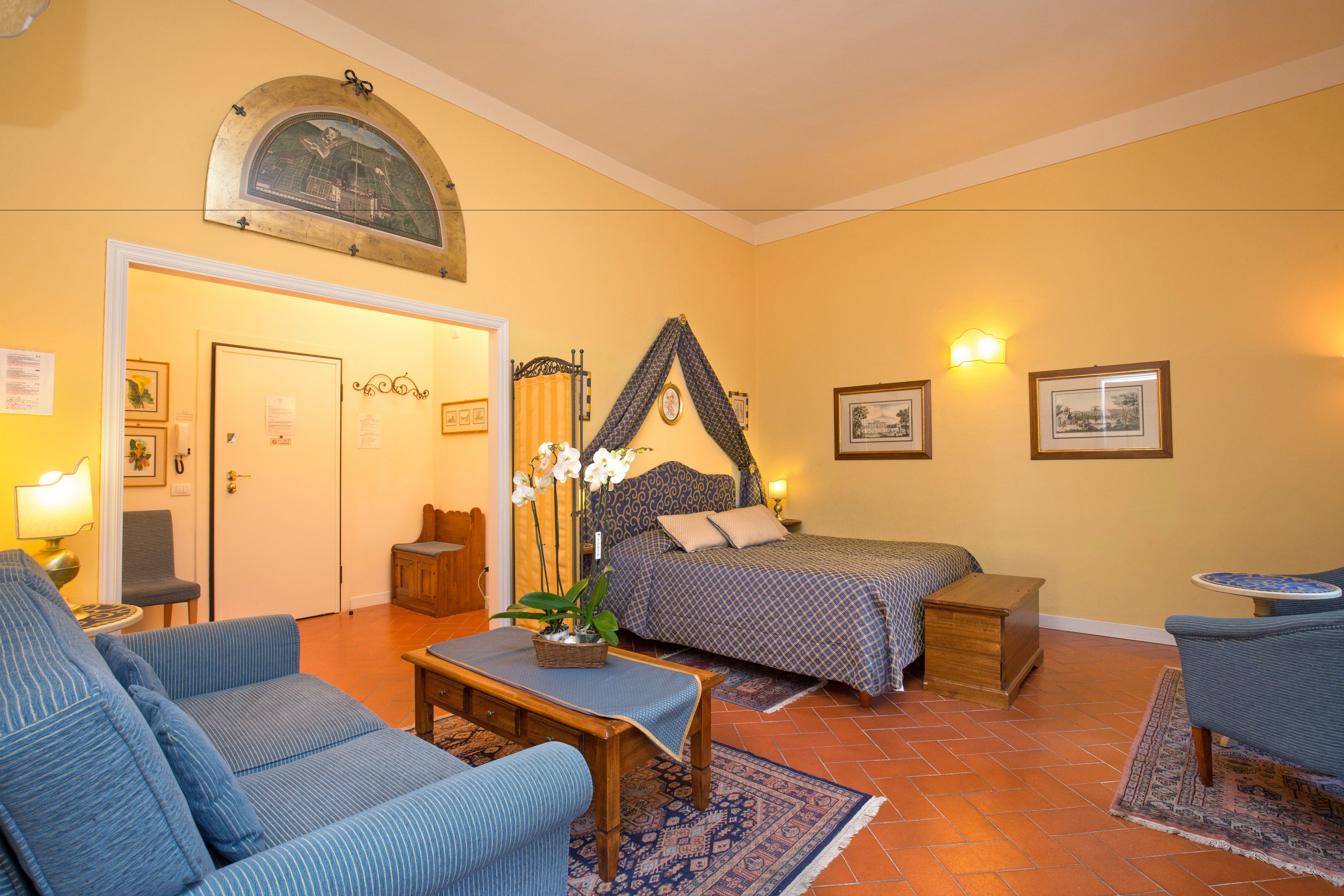 Una habitación con cama, dos sillas, una mesita, lámpara y un adorno en la pared.