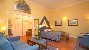 Una habitación con cama, dos sillas, una mesita, lámpara y un adorno en la pared.