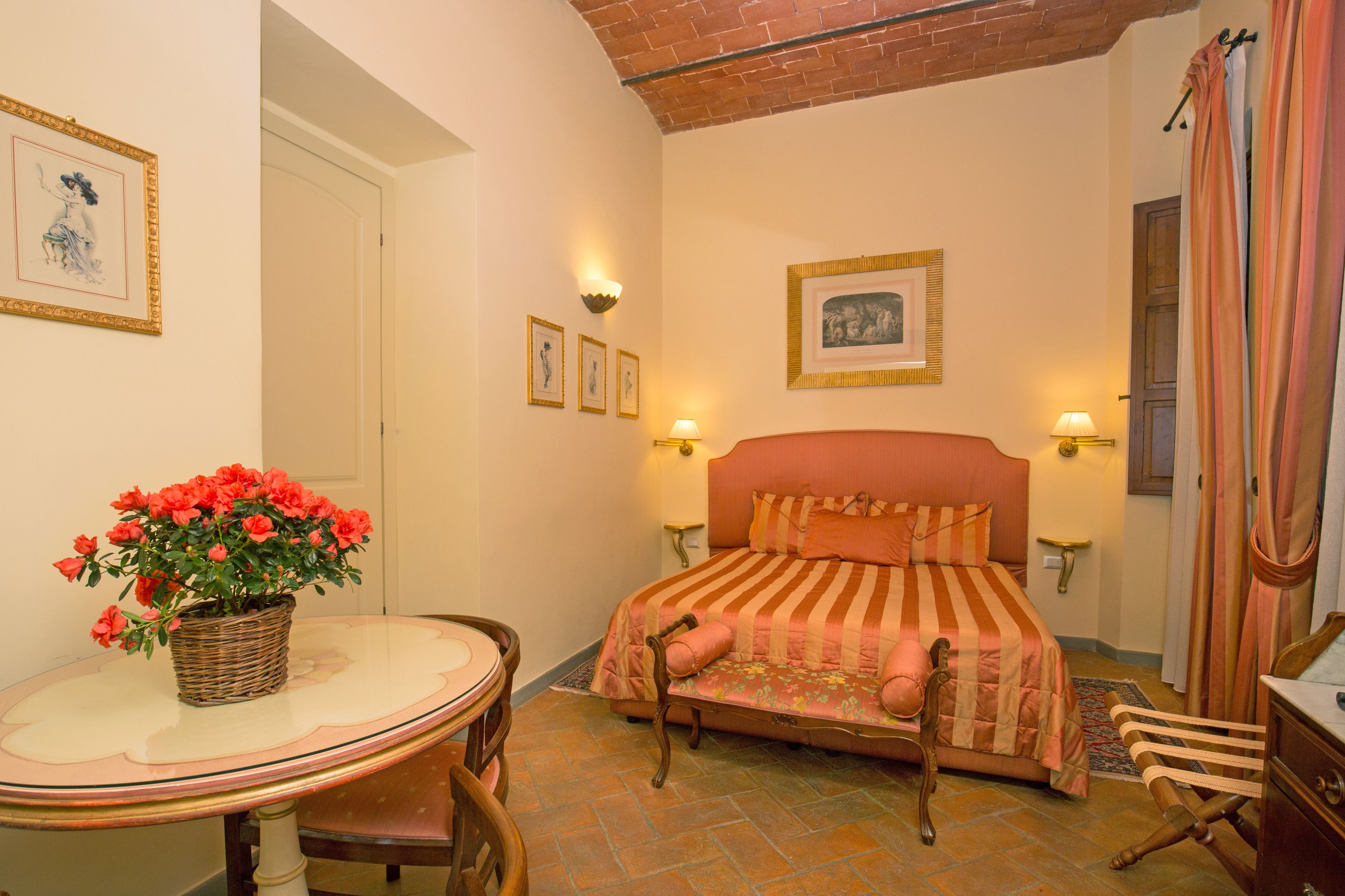A bedroom with a bed, a table with a vase of flowers, and a chair.