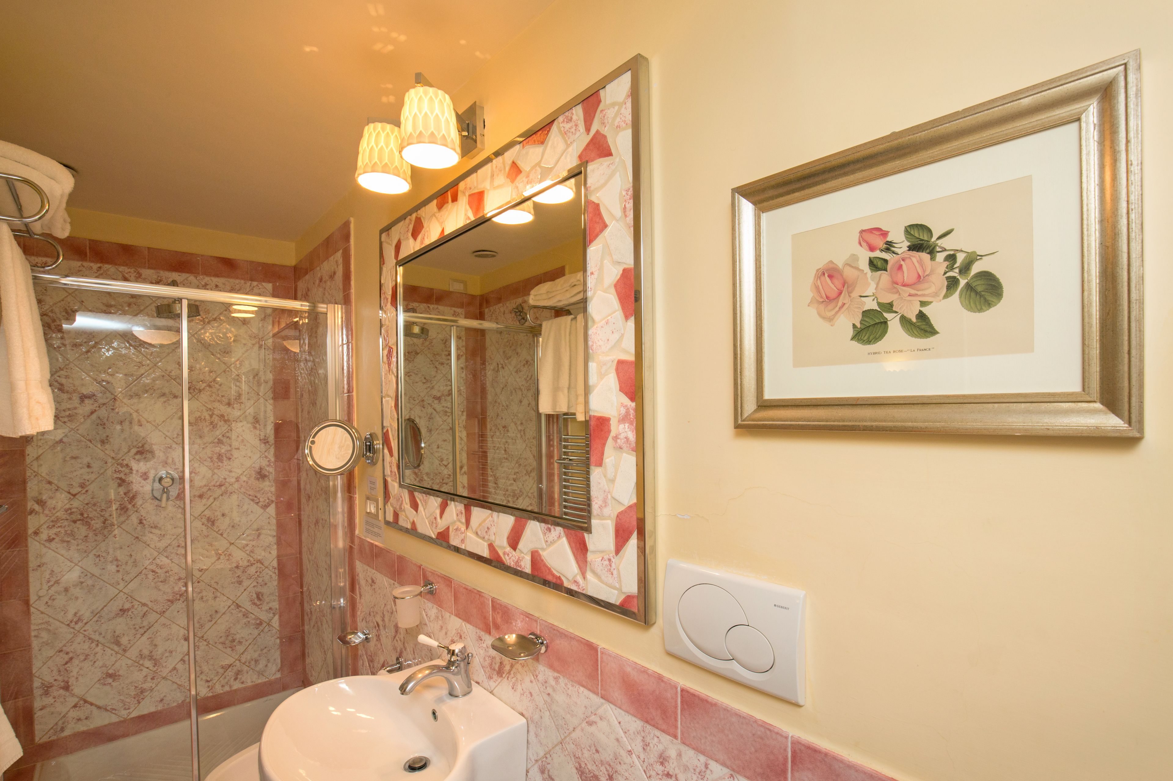 Uma casa de banho com cabine de duche em vidro, lavatório, uma obra de arte floral emoldurada e espelho com moldura decorativa.