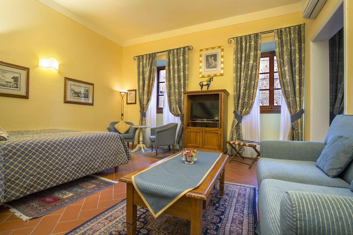 Une chambre d’hôtel avec deux lits, un canapé, une télévision et une petite table sur laquelle se trouve un vase.