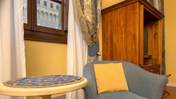 A room with a patterned rug, a blue armchair with a yellow pillow, a wooden cabinet, and a window with curtains.