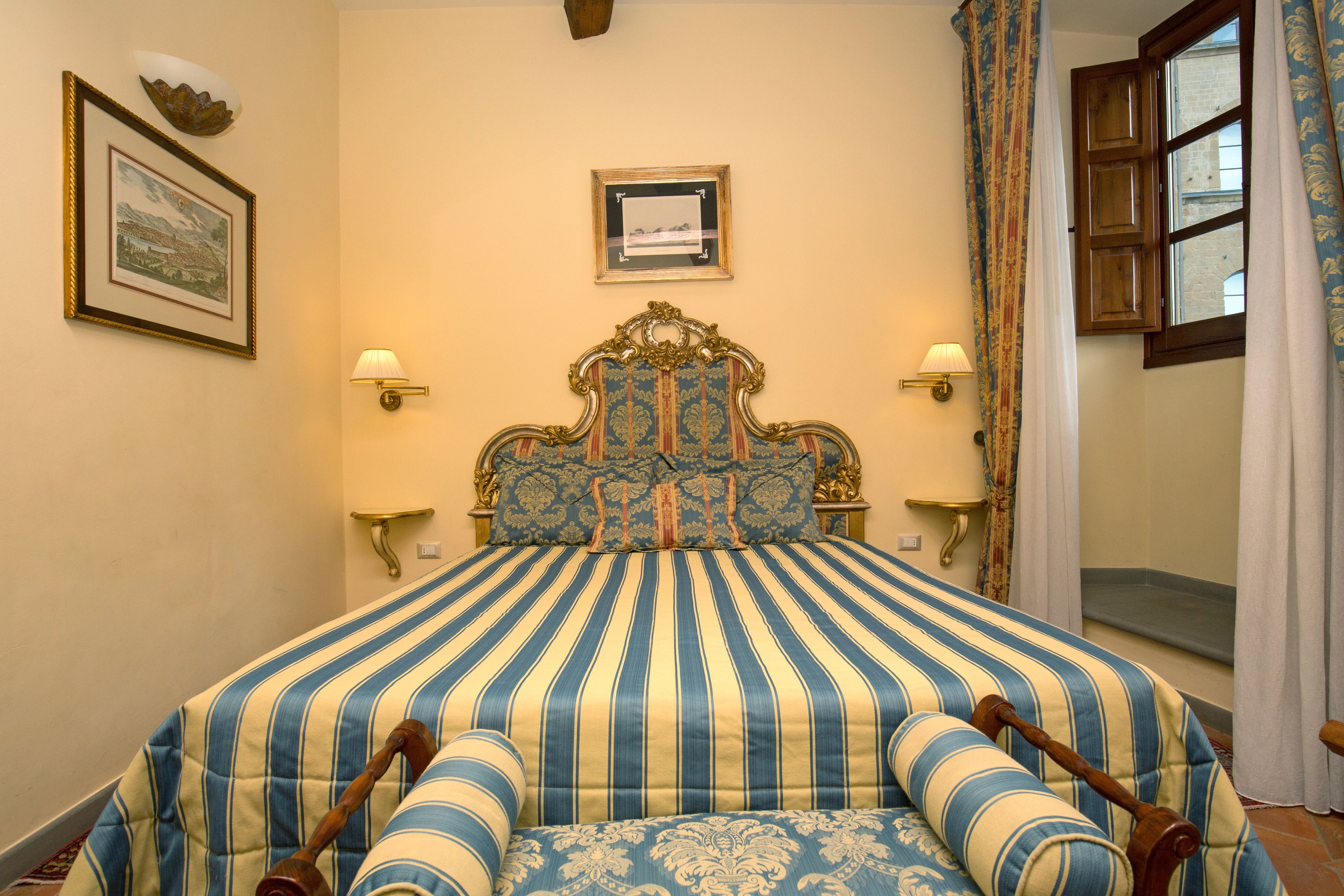 A bed with a striped bedspread, two wall-mounted lamps, and a framed picture on the wall.