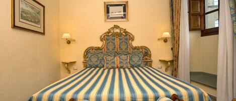 A bed with a striped bedspread, two wall-mounted lamps, and a framed picture on the wall.