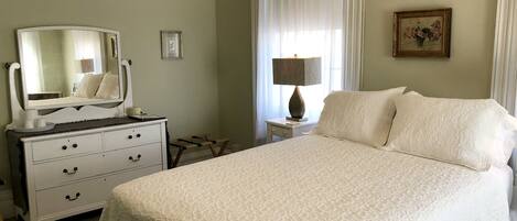 Un dormitorio con cama, cómoda, espejo, lámpara y un cuadro en la pared.