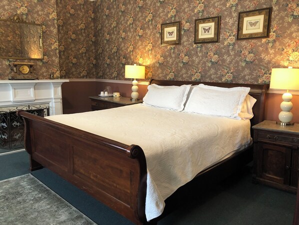 A bedroom with a wooden bed, two bedside lamps, a nightstand, a dresser, a mirror, and floral wallpaper.