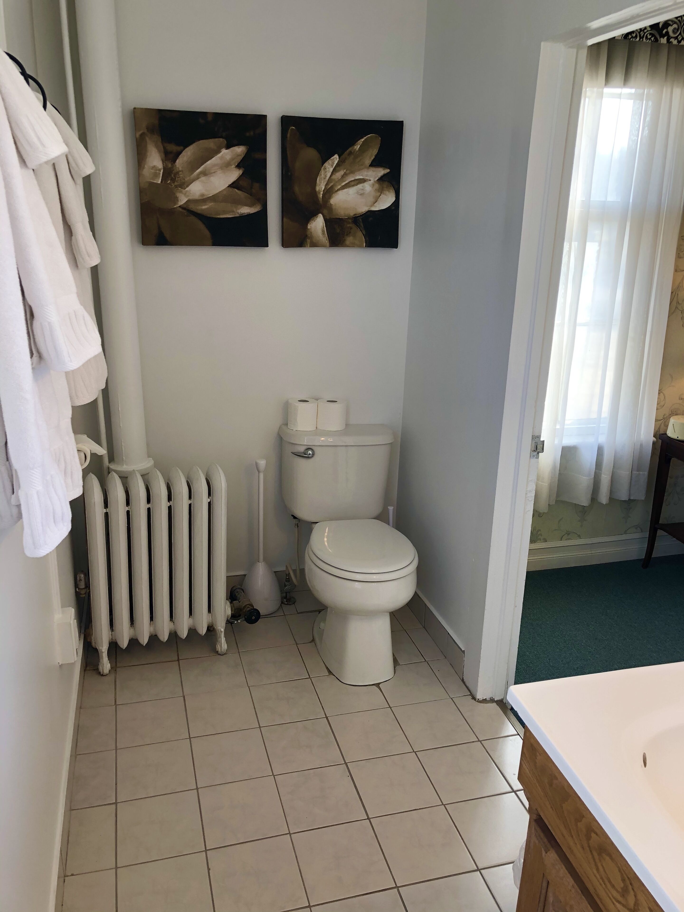 A bathroom with a toilet, radiator, and two wall-mounted flower paintings.