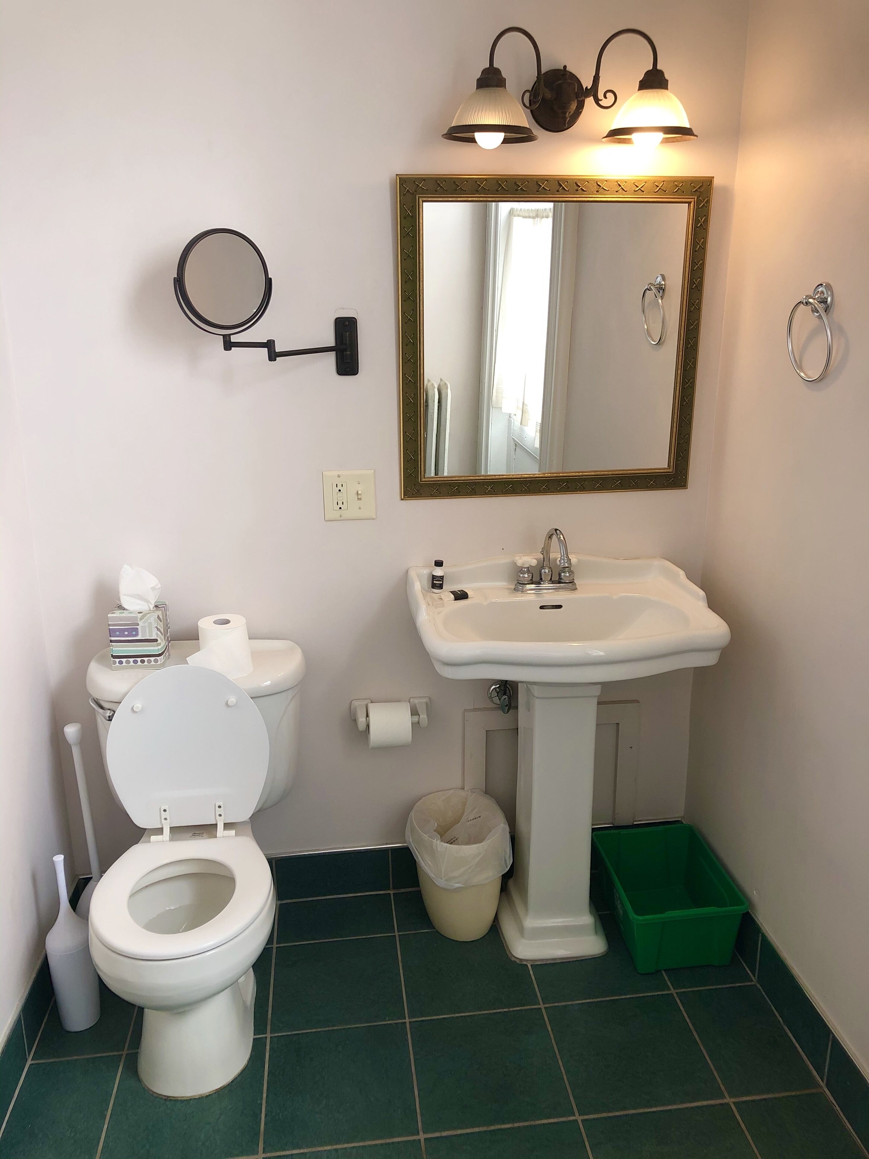 A bathroom with a toilet, sink, mirror, and two wall-mounted lights.