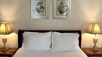 A neatly made bed with white linens, flanked by two bedside tables with lamps, and two framed botanical prints on the wall.