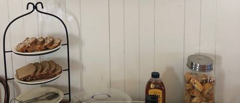 A rustic sign reading "TOURIST HOME" above a table with bread, muffins, butter, jam, and honey.
