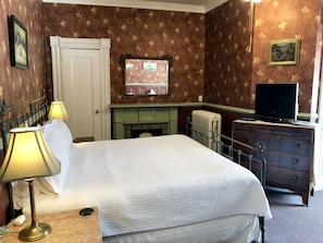 A hotel room with a bed, bedside lamps, a dresser, a television, and a fireplace.