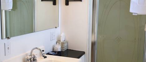 A bathroom with a white sink, wooden vanity, two wall-mounted mirrors, and a glass shower enclosure.
