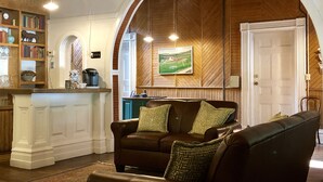 A cozy living room with a brown leather sofa, a coffee table, and a bookshelf filled with books. - Rogues' Harbor Inn (Lansing)