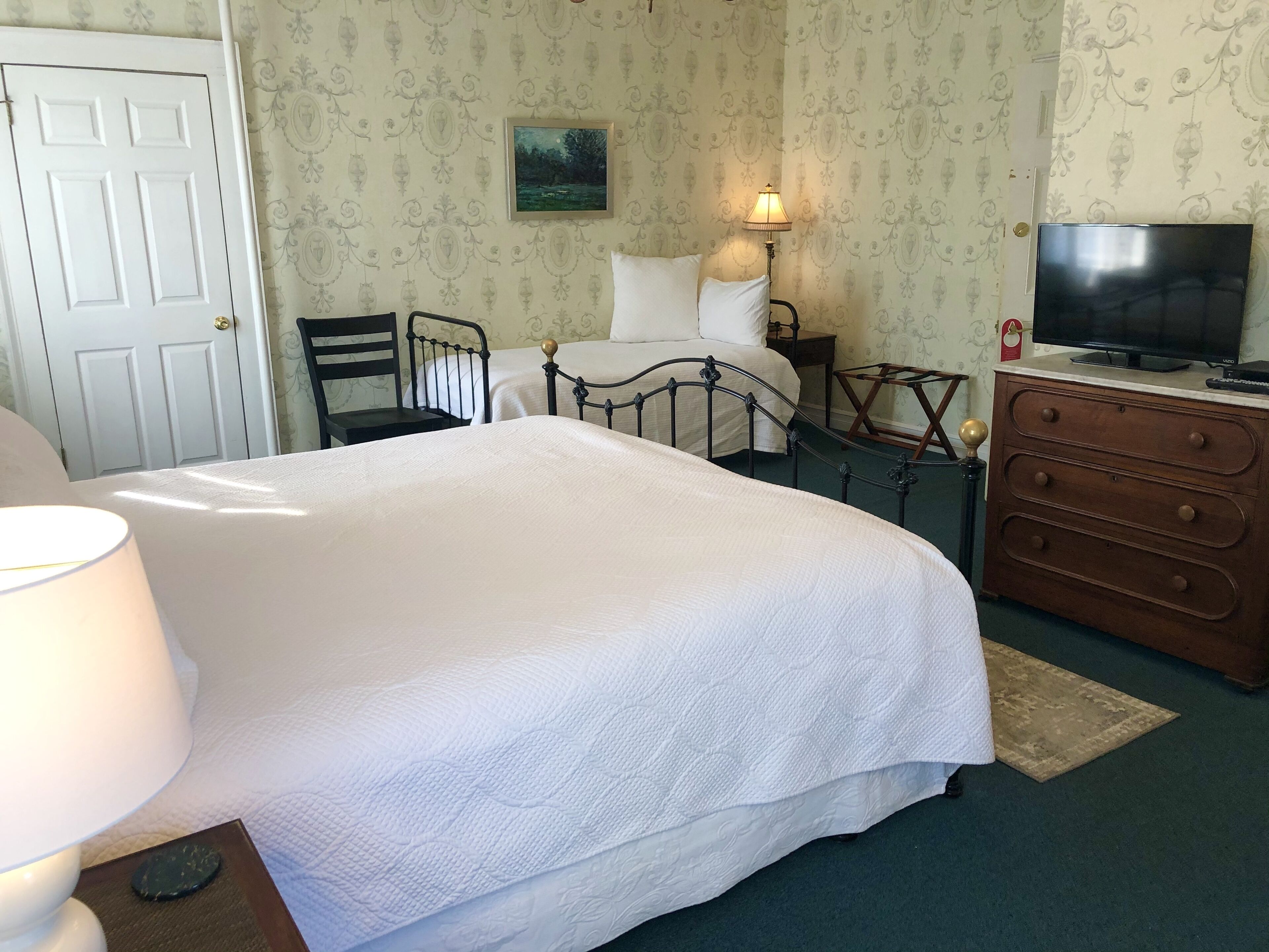 Ein Schlafzimmer mit einem Bett, einem Sessel, einem Schminktisch, einem Fernseher und einer Lampe.