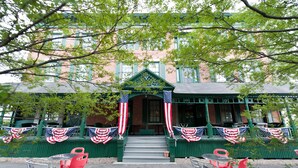 A building with green shutters, a porch with red chairs, and American flags. - Rogues' Harbor Inn (Lansing)