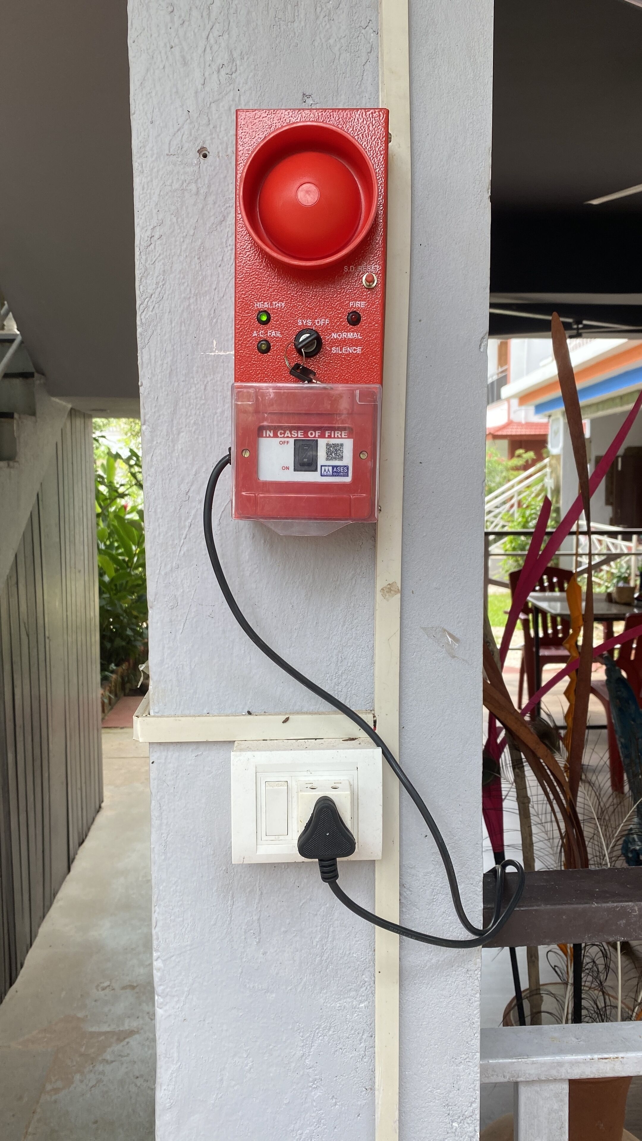 Painel de controle de alarme de incêndio fixado em parede, ligado a uma tomada.