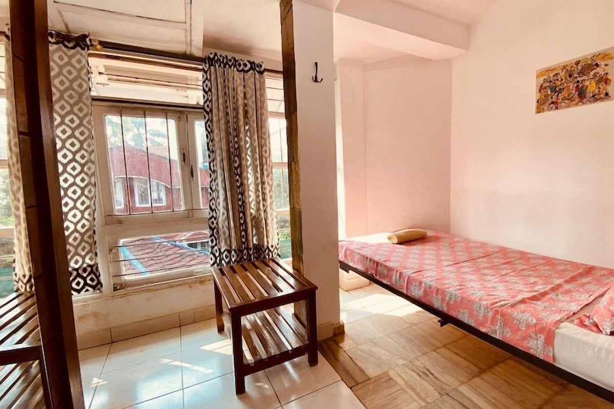 Una habitación con una cama, un banco, una ventana con cortinas y un cuadro en la pared.