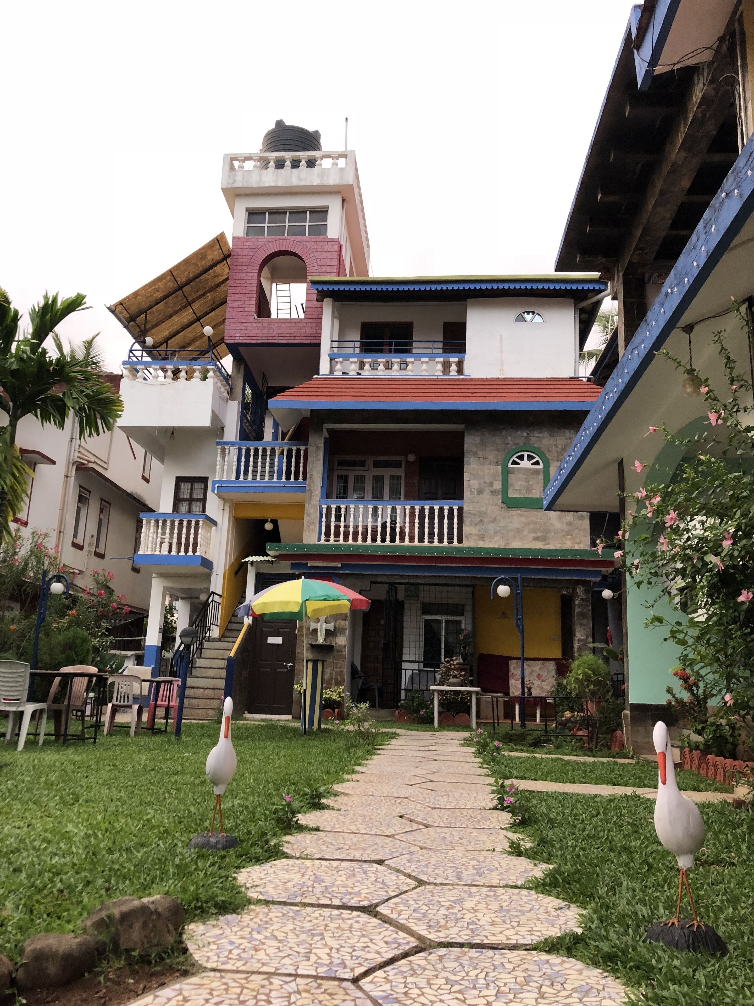Un edificio de varios pisos con una entrada central, una escalera y un pequeño área al aire libre con sillas y una sombrilla.