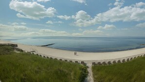 Een strand met een zandpad dat naar het water leidt, een rij stoelen langs de rand, en een grasveld op de voorgrond.